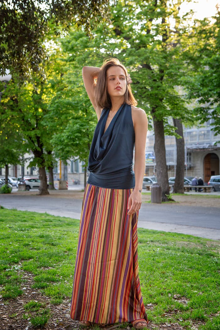 Woman posing in a park wearing a colorful skirt and blouse on a sunny day.
